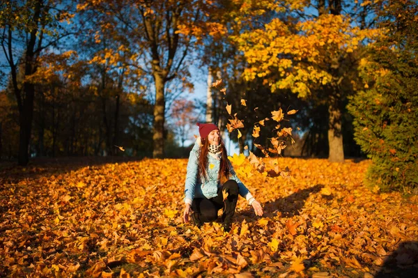 Felicità concetto di svago spensierato. Donna dai capelli lunghi dai capelli rossi che si rilassa nel parco autunnale vomitando foglie in aria. Bella ragazza in foresta arancione fogliame all'aperto — Foto Stock