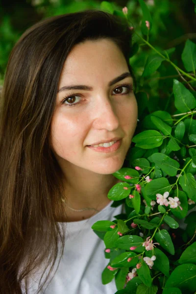 Joven chica hermosa cerca de las flores. Fotón verde y flores. Retrato de una joven hermosa chica cerca de las flores. Retrato de una joven hermosa mujer, cara bonita de cerca, grandes labios rosados, pelo liso dr — Foto de Stock