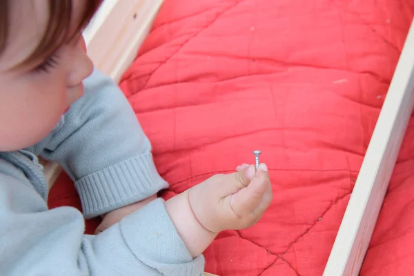 Criança segura um parafuso. Fechar as mãos crianças segurando parafuso na placa de madeira. Aula de artesanato no jardim de infância. Conjunto de ferramentas na mesa . — Fotografia de Stock