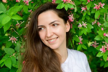 Çiçeklerin yanında güzel bir kız. Foton yeşili ve çiçekler. Çiçeklerin yanında güzel bir kızın portresi. Genç güzel bir kadının portresi, güzel bir yüz yakın plan, büyük pembe dudaklar, düz saçlar.