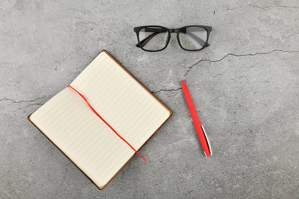 Gafas con cuaderno sobre fondo gris. Escritorio de oficina con accesorios de negocios. Vista superior —  Fotos de Stock
