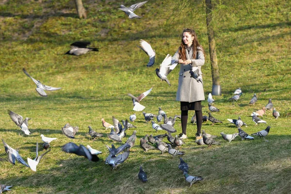 Chica alimenta palomas. en el parque en una pagoda soleada. cuidar de los animales. Hermosa mujer sonriente alimentando palomas en el parque durante el día —  Fotos de Stock