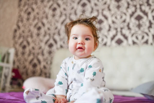 Baby poseert op camera zittend op het bed. Het kind speelt in het beddengoed. — Stockfoto