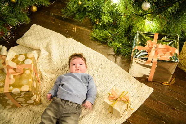 Child near christmas tree top view. Closeup portrait of smiling cute little child in holiday christmas interior near festive tree. Top view of happy kid laying on white wooden floor near presents unde — Stock Photo, Image