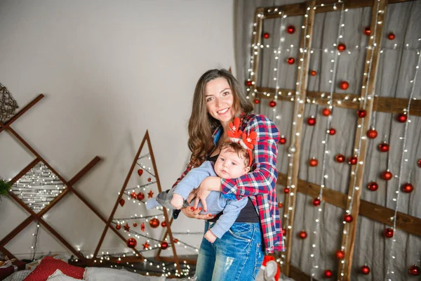 Mom and baby hug at the Christmas tree. Happy baby and his mom are looking at the frame. Mom with son hugging for Christmas. and have fun. newborn baby for the new year.