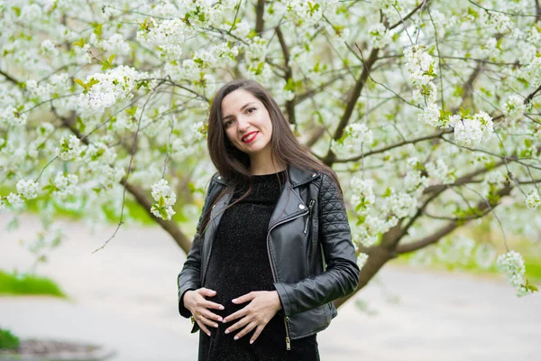 Schwangere Mädchen in der Nähe der blühenden Apfelbäume. Schwangere mit langen Haaren im Stehkleid — Stockfoto