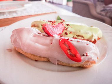 Beyaz bir tabakta renkli jöleli ekler. Ev yapımı ekekler. Geleneksel ekler, klasik profesyoneller, eklairlerin Fransızcası. Fıstık, vanilya, jöleli çilek. Tahta bir masada.