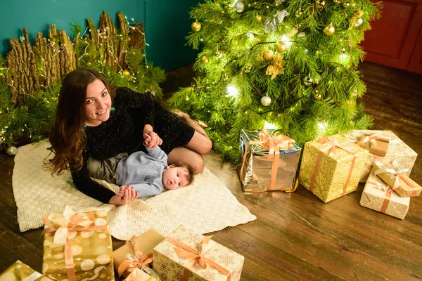 Weihnachten und Muttertag. Weihnachten und Menschen Konzept - Mutter und Baby mit Geschenken. vor weihnachtlichem Hintergrund. Warme Weihnachten. — Stockfoto