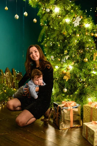 Baby with mother at Christmas. happy family mother and baby little son playing home on Christmas holidays. New Year's holidays. Toddler with mom in the festively decorated room with Christmas tree. Po — Stock Photo, Image