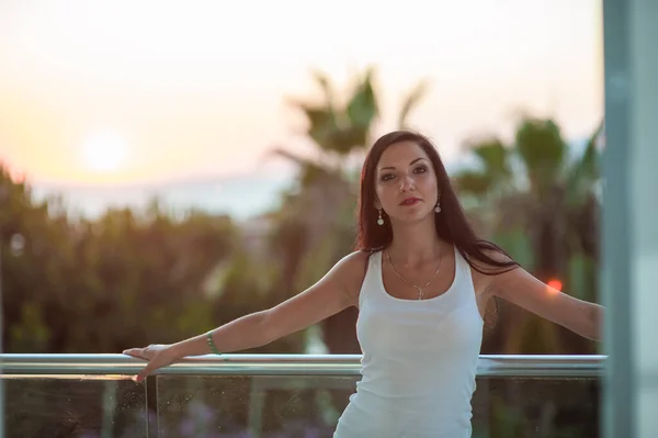 La chica en el fondo de la puesta de sol del mar. hermosa morena al atardecer vacaciones en el mar disfrutando del cálido sol. hermosa modelo exterior con el sol en el fondo en una camiseta blanca — Foto de Stock