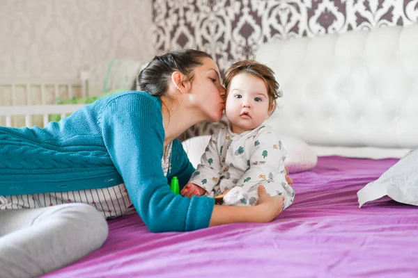 Mom and love for the child. on the bed. emotions of happiness. kissing baby and hugging. Pretty woman holding a newborn baby in her arms — Stock Photo, Image