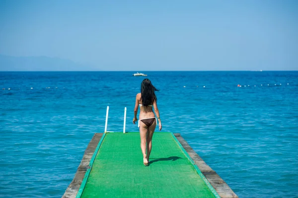 La ragazza va lungo il molo fino al mare, molo verde. Giovane donna. concetto di viaggio — Foto Stock