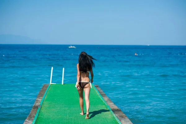 La ragazza va lungo il molo fino al mare, molo verde. Giovane donna. concetto di viaggio — Foto Stock