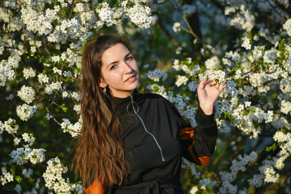 Niña sobre un fondo de un árbol de floración blanca. Retrato al aire libre de joven hermosa dama elegante de moda con el pelo largo, con sombrero de paja, blusa vintage, pendientes azules, posando en la floración ap — Foto de Stock