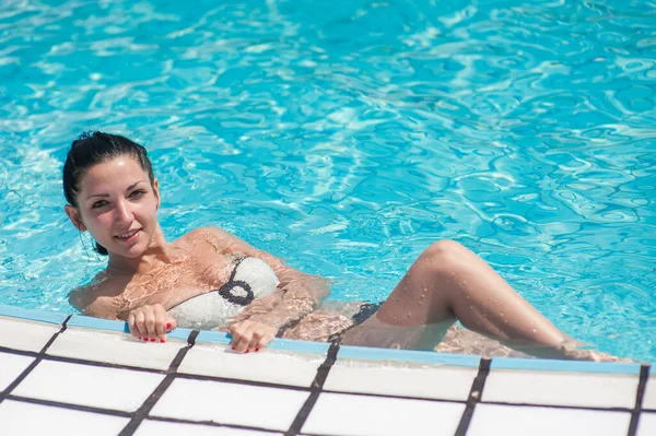 Girl resting in the pool. Portrait of a girl in the pool. Young brunette bathed by the pool at the hotel. The girl is resting and relaxing. Sunburn on a sunny day. — Stock Photo, Image