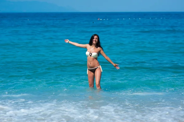 Hermosa chica con cuerpo perfecto en bikini bañador jugando con agua en la playa de las Maldivas. Joven modelo delgado con piel bronceada divirtiéndose en el océano. Nubes y cielo en el fondo. Colorf — Foto de Stock