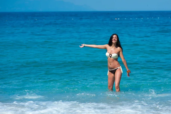 在马尔代夫海滩上，身穿比基尼泳衣、身材完美的美女正在与水玩耍。 年轻的身材苗条的模特，有着晒黑的皮肤，在海里玩的很开心。 背景上的云彩和天空. 彩色f — 图库照片