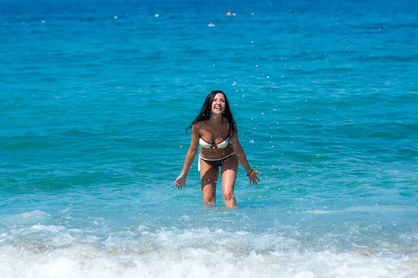 Menina bonita com corpo perfeito em biquíni maiô brincando com água na praia das Maldivas. Modelo jovem e magro com pele bronzeada se divertindo no oceano. Nuvens e céu no fundo. Colorf — Fotografia de Stock