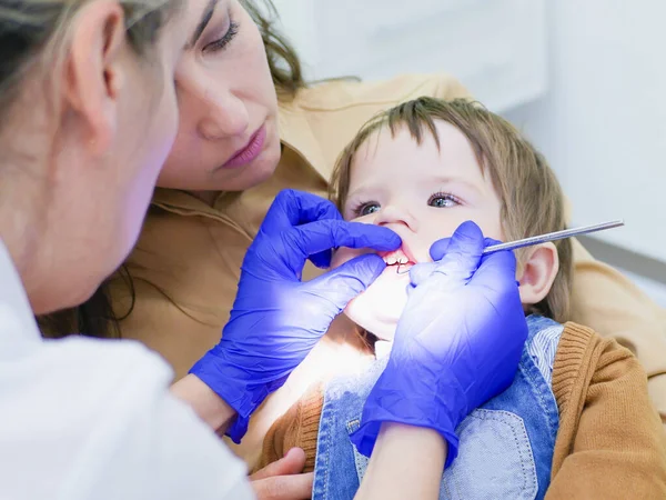Doktor küçük bir çocuğun dişlerine bakar. Bebek, annenin kollarında oturuyor. Klinikte dişçi çocuğun dişlerini inceliyor. Dişçi koltuğundaki küçük bir hasta gülümsüyor. Dansçı dişleri tedavi eder. Kapat