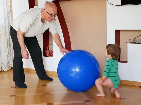 那孩子和爷爷一起玩一个球。 在家里打一个大蓝球。 一个男孩在和他的祖父玩. — 图库照片