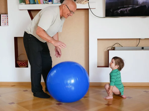 Barnet leker med morfar en boll. spela en stor blå boll hemma. En pojke leker med sin farfar. — Stockfoto