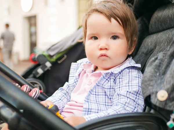Bebê sentado em um carrinho cinza. segurando um brinquedo nas mãos. Um passeio quente para o bebê . — Fotografia de Stock