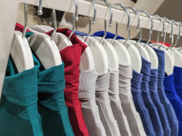 clothes on hangers in the store. Clothes hang on a shelf in a designer clothing store in different colors.