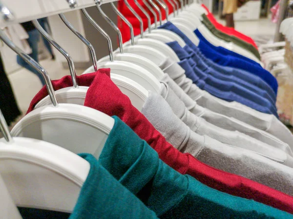 Ropa en perchas en la tienda. Ropa colgada en un estante en una tienda de ropa de diseño en diferentes colores . — Foto de Stock