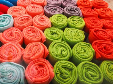 çok renkli havlular bir tüpe sarılmış ve raflarda yatıyorlar. Çok renkli kumaş bir tüpe sarılmış.