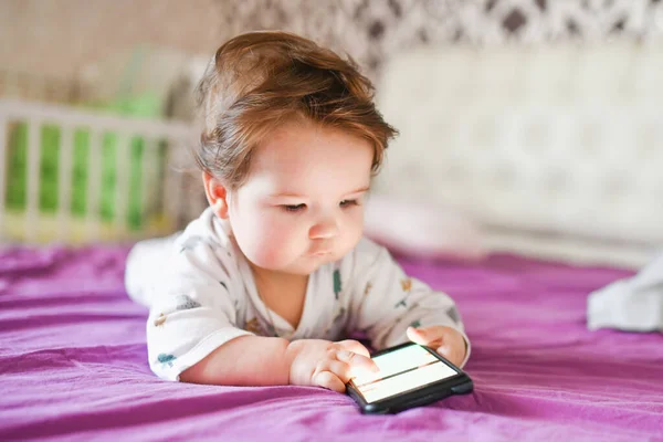 Child addiction to phones. radiation from the phone to the child. A little boy 0-1 years old with a smartphone in his hands looks at the screen with enthusiasm. Child gadget addiction