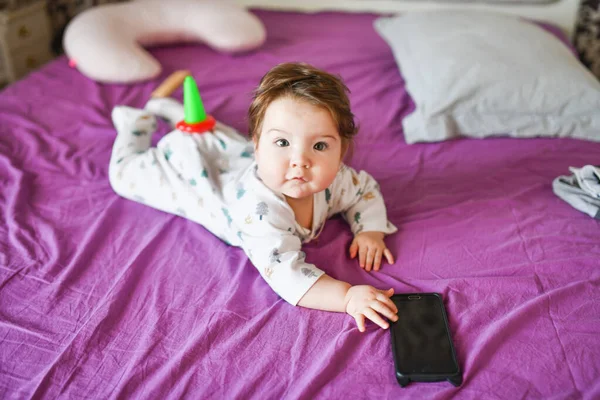 Dětské a mobilní zařízení. Holčička v posteli se dívá na smartphone — Stock fotografie