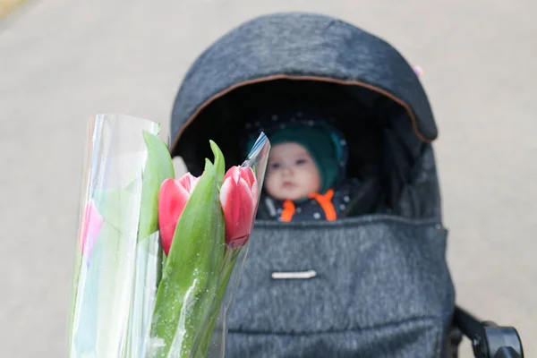 Цветы молодые матери. С Днем матери Маленький ребенок поздравляет мам и дарит ей цветы красных тюльпанов. День благодарения за ребенка — стоковое фото