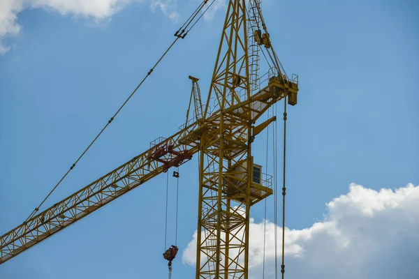 High-rise construction crane with a long arrow of yellow color against the blue sky over a new multi-storey building of concrete and brick under construction — ストック写真