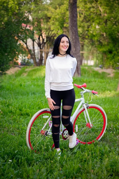 Hermosa chica posando en una bicicleta. bicicleta blanca y roja. caminar en la naturaleza. estilo de vida saludable. fin de semana en la naturaleza Retrato de una hermosa chica feliz en una camiseta blanca. lugar para escribir — Foto de Stock