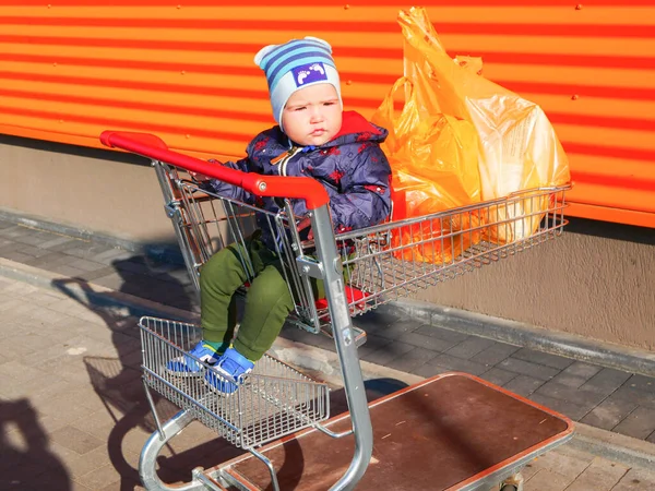 baby on a shopping trolley. Baby boy sitting in a shopping trolley outside. On orange background