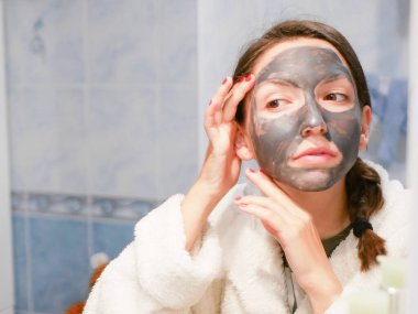 Kozmetik siyah maske. Kadın yüzüne güzellik getiriyor, siyah noktalardan kurtuluyor, siyah bir maske kullanıyor. Banyoda bir kadın aynaya bakıyor. 