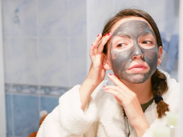 Kozmetik siyah maske. Kadın yüzüne güzellik getiriyor, siyah noktalardan kurtuluyor, siyah bir maske kullanıyor. Banyoda bir kadın aynaya bakıyor. 