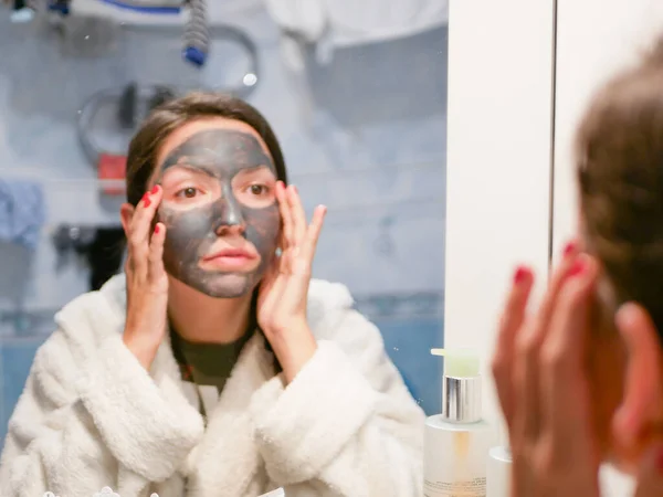Girl and face mask. Woman with clay carbo black mask on her face. The girl takes care of oily skin. Cosmetic procedures. Skin care. — Stock Photo, Image