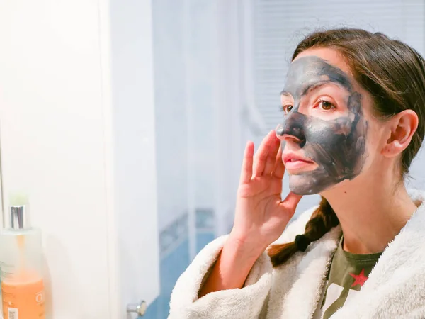 Girl cares for oily skin. Cosmetic procedures. Skin care. Young woman with a black mud mask on her face. cleansing pores. Cosmetic procedures. — Stock Photo, Image