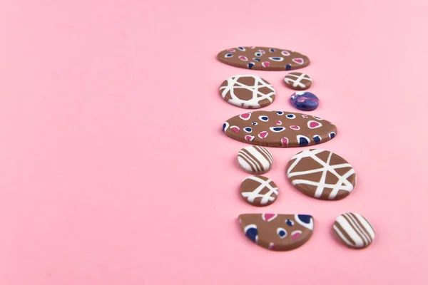 A product from polymer clay. Hand sculpting, product for earrings on a pink background. View from above. Beige earrings with colorful patterns. Handmade polymer clay jewelry