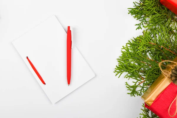 Blank white notebook and red pen on christmas white background. Christmas fir branches, cones, gifts. Letter to Santa Claus, mock up. Blank white notebook and red pen on white