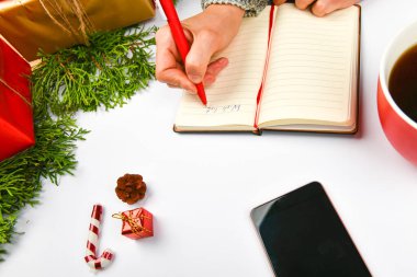 Kahve fincanıyla dilek tutuyor. Hedeflerin hayalleri, yılbaşı konseptini deftere yazmak için bir liste oluşturur. Yılbaşı bayramında köknar dallarıyla arka planda kalan bir kadın.