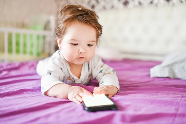 Детская зависимость от телефонов. излучение от телефона ребенку. Маленький мальчик 0-1 лет со смартфоном в руках с энтузиазмом смотрит на экран. Детская гаджетная зависимость — стоковое фото