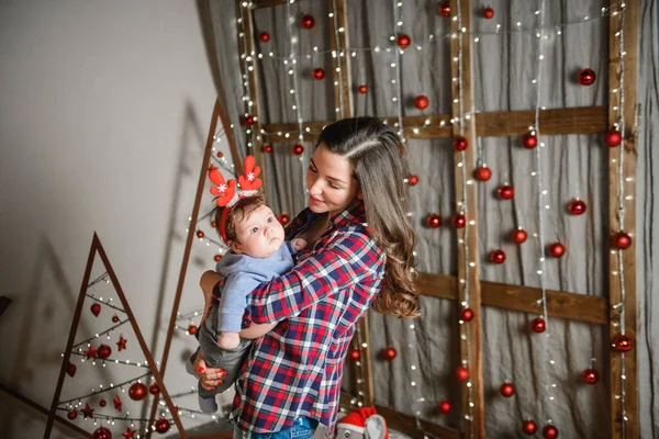 Noel ağacında anne ve bebek kucaklaması. Mutlu bebek ve annesi çerçeveye bakıyorlar. Noel'de oğluyla birlikte anne kucaklıyor. ve eğlenin. yeni yıl için yenidoğan bebek. — Stok fotoğraf