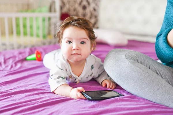 Dítě s telefonem. na postel. znalost mobilních zařízení. Dítě s mobilním telefonem. Malé dítě v ležérní barevné pruhované oblečení s mobilním telefonem — Stock fotografie