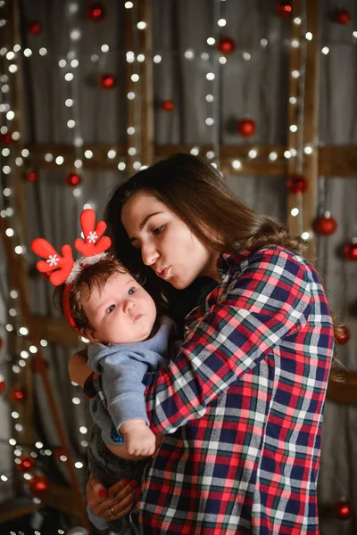 Mom and baby hug at the Christmas tree. Happy baby and his mom are looking at the frame. Mom with son hugging for Christmas. and have fun. newborn baby for the new year.