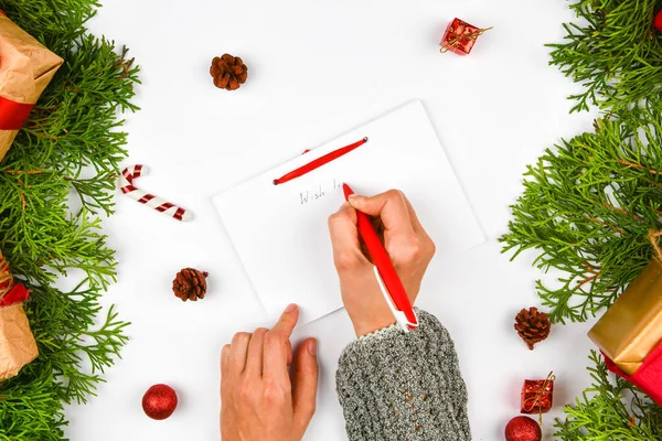 Wishes for next year. Woman hand on the background of fir branches. New Year\'s winter holiday. To-do list on a notepad next to Christmas decorations, pine cones and a coffee mug. Layout concept, New Y