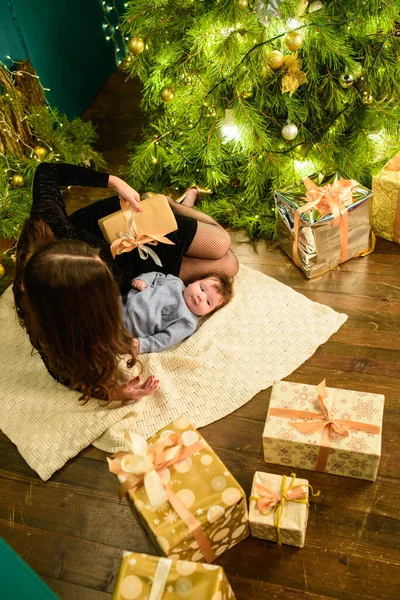Mutter und Baby umarmen sich am Weihnachtsbaum. Glückliches Baby und seine Mutter betrachten den Rahmen. Mutter mit Sohn beim Umarmen zu Weihnachten. und Spaß haben. Neugeborenes für das neue Jahr. — Stockfoto
