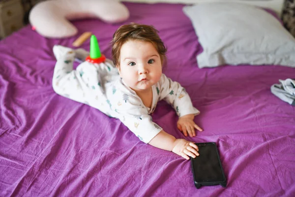 Dítě s telefonem. na postel. znalost mobilních zařízení. Dítě s mobilním telefonem. Malé dítě v ležérní barevné pruhované oblečení s mobilním telefonem — Stock fotografie