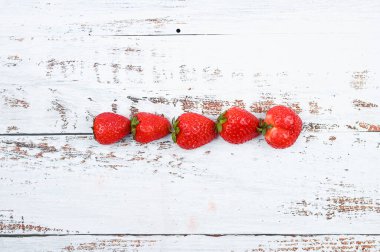 Beyaz ahşap arka planda dizilmiş kırmızı çilekler..